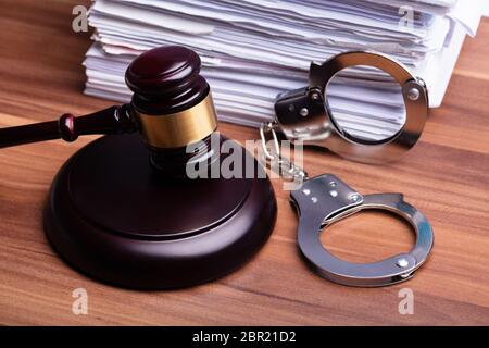 Close-up Of Gavel And Handcuffs Near Stacked Paper On Wooden Table Stock Photo