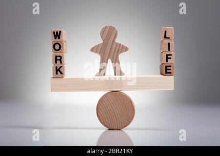 Human Figure Balancing Between Work And Life On Wooden Seesaw Against Gray Background Stock Photo