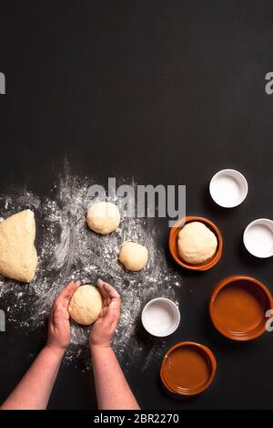 Top view with woman's hands shaping the dough to make bread buns. Baking bread in small round ceramic trays. Stock Photo
