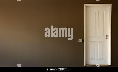 Light switch on the gray textured wall next to the white door with metallic handle Stock Photo