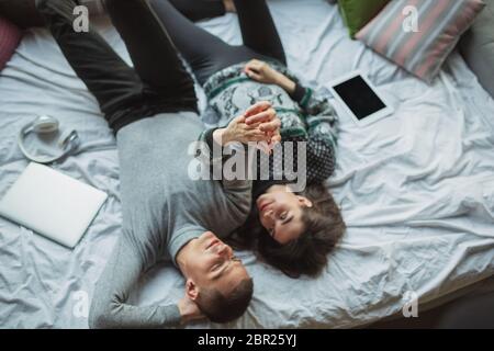 Lying down, lovely. Quarantine lockdown, stay home concept - young beautiful caucasian couple enjoying new lifestyle during coronavirus worldwide health emergency. Happiness, togetherness, healthcare. Stock Photo