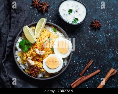 Indian Egg Biryani or anda rice top view on dark background. Egg Biryani - Basmati rice cooked with masala roasted eggs and spices, served with yogurt Stock Photo