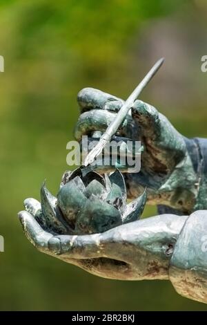 part of a statue of hands holding water lily and paint brush dusting the pollen for propagation Stock Photo