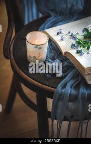 Cozy moment with a candle, a book and forget me not flowers on a chair Stock Photo