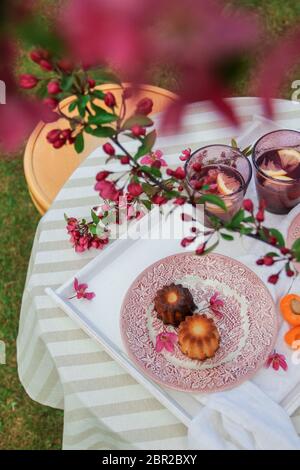 Colorful spring table setting in the garden under the blooming crab apple tree. Enjoying caneles and some drinks Stock Photo