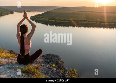 Happy young woman practicing yoga at sunset. Healthy active lifestyle concept Stock Photo