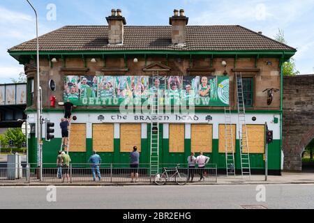 Gorbals, Glasgow, Scotland, UK. 20th May, 2020. Despite being closed due to the coronavirus pandemic The Brazen Head still celebrated Celtic becoming Scottish Premiership Champions for the 9th season in a row. Picture shows banner saying 'Celtic F.C 9 in a Row' being erected as locals watch on Credit: Kay Roxby/Alamy Live News Stock Photo