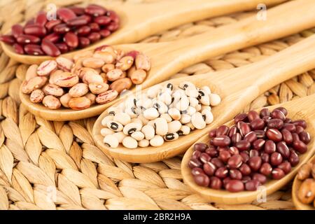 Various beans in the wooden spoons on the beige background. Stock Photo