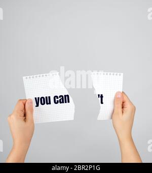 two hands holding a paper torn in half, inscription you can’t , gray background, conceptual and motivating gesture Stock Photo