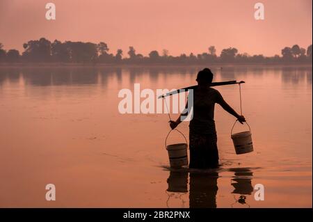 Young Cambodian woman collects water at twilight in Srah Srang, an ancient reservoir at Angkor. Siem Reap Province, Cambodia, Southeast Asia Stock Photo