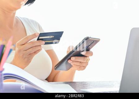 Woman use credit card for online shopping on smart phone and laptop ,shopping from home,focus on credit card Stock Photo