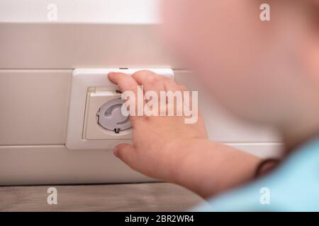 Baby Girl Playing With Electrical Extension On Floor At Home Stock Photo