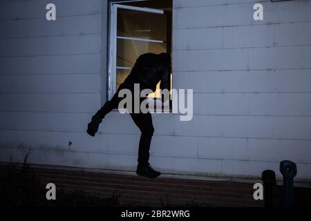 Rear View Of A Burglar Entering In A House Through A Window Stock Photo