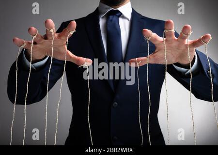 Man's Hand Controls The Puppet With The Fingers Attached To Threads Against Gray Background Stock Photo