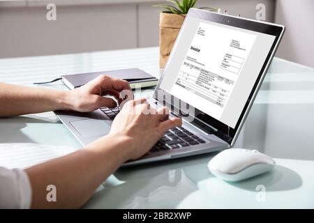 Close-up Of A Businesswoman's Hand Checking Invoice On Laptop Stock Photo