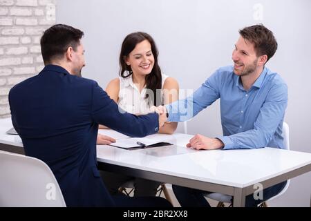 Close-up Of Advisor Handshaking With A Smiling Young Couple After Deal Stock Photo