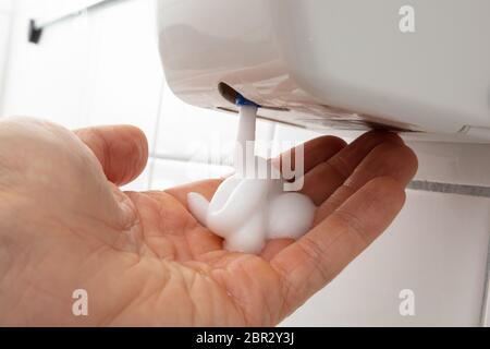 Close-up Of Person's Hand With Liquid Soap Dispenser On Tiled Wall Stock Photo