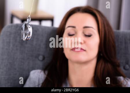 Attractive Young Woman Being Hypnotized While Sitting On Sofa At Home Stock Photo