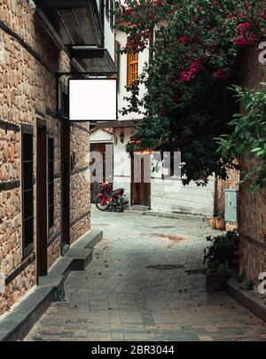 Narrow street in Antalya’s old town with rectangular billboard White mockup on the wall.  Old town in city centrum is a must see place for tourists. Stock Photo