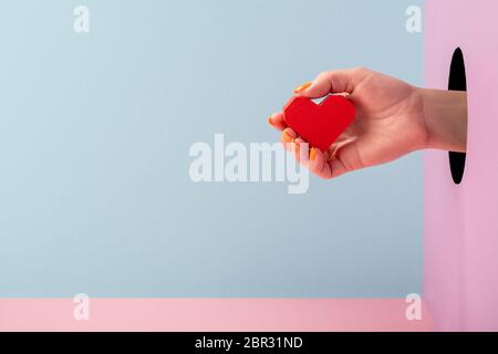 Woman's hand holding a red paper heart on blue and pink background Stock Photo