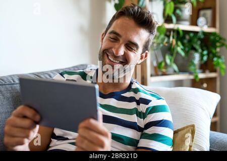 Laughing young man using a digital tablet on his sofa Stock Photo