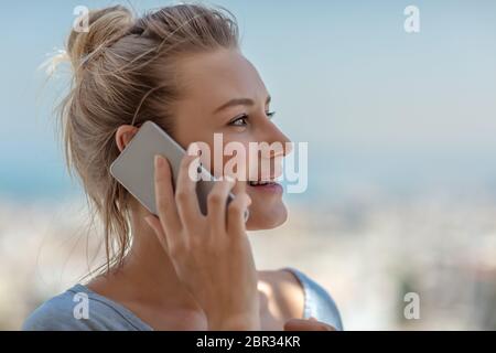 Portrait of a cute blond woman talking on the phone outdoors, enjoying communication, using mobile phone, modern device Stock Photo