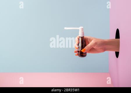 Woman's hand holding a bottle of throat spray on blue and pink background Stock Photo