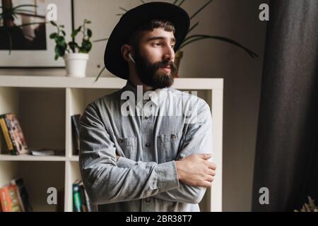 Close up of a handsome young hipster man wearing wireless earphones while standing at the office Stock Photo
