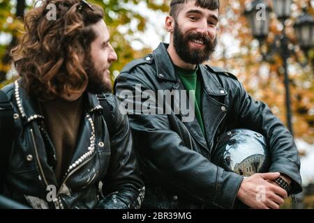 Photo of handsome joyful men bikers smiling and talking while standing on autumn street Stock Photo