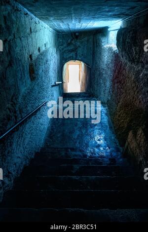 Glomy passage with stairs carved in stone with light at the end of a tunnel, creepy urban corridor to the waterfront in city of Valletta, Malta Stock Photo