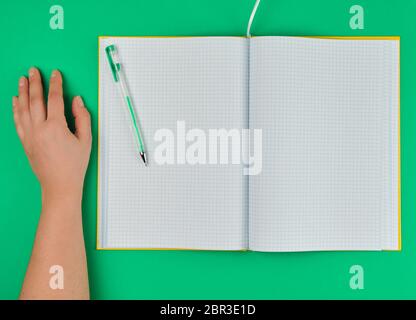open checked notebook and female hand, top view, green background Stock Photo