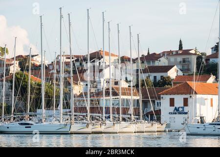 Looking towards the Trogir marina and island of Ciovo, with several sailboats docked in front of ACI Club Trogir, and medieval residences close by. Stock Photo