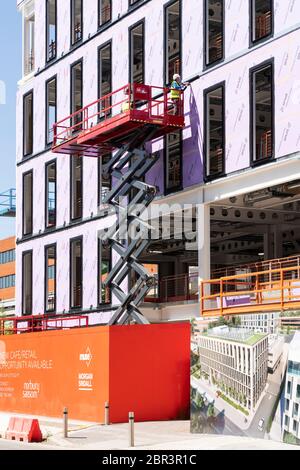 Workmen on a mewp (mobile elevated working platform) cherry picker fixing cladding to a new office building on Basing View in Basingstoke, UK Stock Photo