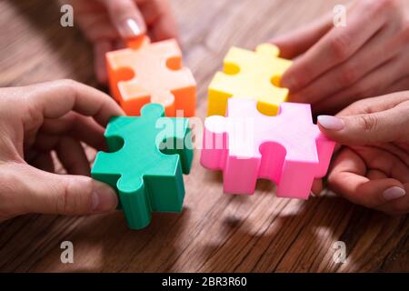 Close-up Of Businesspeople Solving Jigsaw Puzzle Together On Wooden Desk Stock Photo