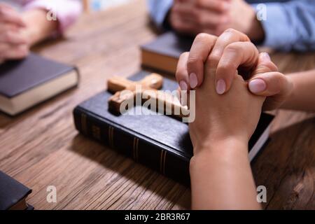 Close-up Of Businesspeople's Praying Hands Over The Bible On Wooden Desk Stock Photo