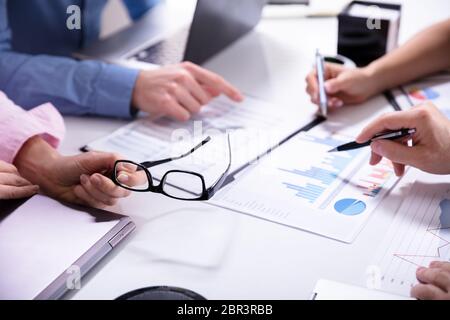 Close-up Of Business Colleagues Working Together With Data Analysis Paper On Desk Stock Photo
