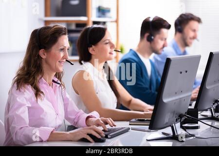 Happy Young Customer Service Executives Using Earphones Working In Call Center Stock Photo