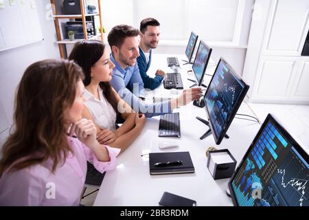 Young Businesspeople Stock Market Broker Analyzing Graph On Computer At Workplace Stock Photo
