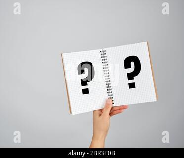 female hand holds open  notepad into a cell on gray background, question mark Stock Photo