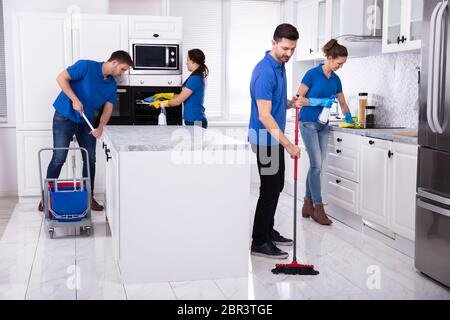 Group Of Young Janitors In Uniform Cleaning Kitchen At Home Stock Photo