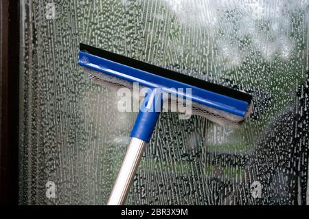 Cleaning window using a squilgee to wash glass. Stock Photo