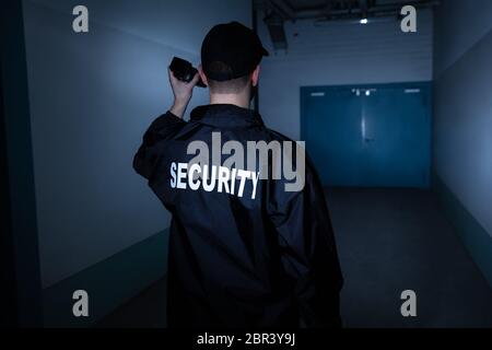 Rear View Of A Male Security Guard With Flashlight Standing In Corridor Stock Photo