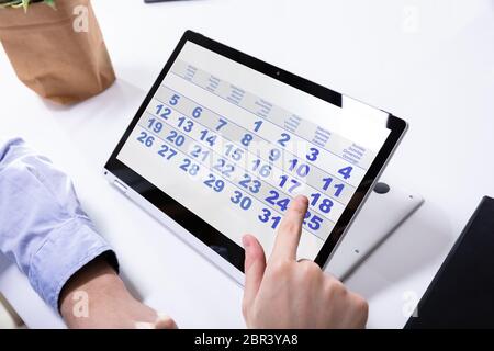 Close-up Of A Businessman's Hand Using Calendar On Laptop Over Desk Stock Photo