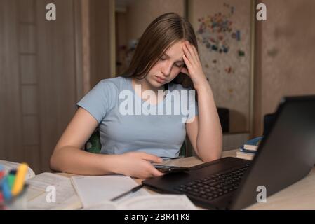 Tired upset teenager girl 12-14 years old. Smartphone in hand, home, laptop lessons, watching videos reading assignments. E-education distance Stock Photo
