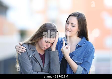 Sad woman being comforted by a bad friend in the street Stock Photo
