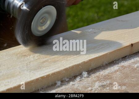 The brushing process of wooden plank. Male hand is holding brushing machine electrical rotating with brush metal disk sanding a piece of wood. Stock Photo