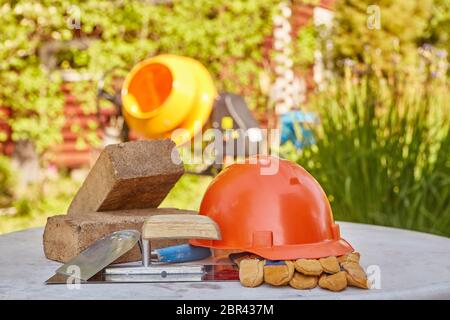Construction concept. Bricks, tools, hard hat, gloves and concrete mixer. Outdoors Stock Photo