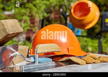 Construction concept. Bricks, tools, hard hat, gloves and concrete mixer. Outdoors Stock Photo