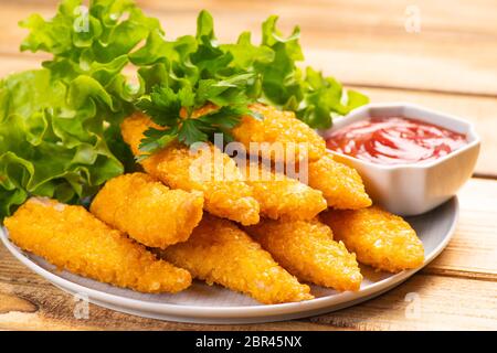 Fast homemade food.Fast food.Chicken breaded nuggets with basil leaves and ketchup on a wooden kitchen board on a wooden table . Stock Photo