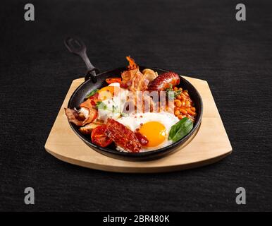 Traditional Full English Breakfast served in cooking pan on black background Stock Photo